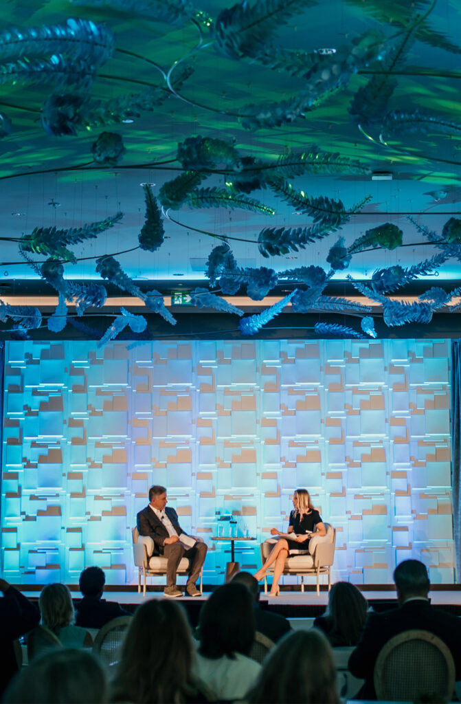 Two people sitting in chairs, talking on the stage in Edgewater at The Pearle Hotel