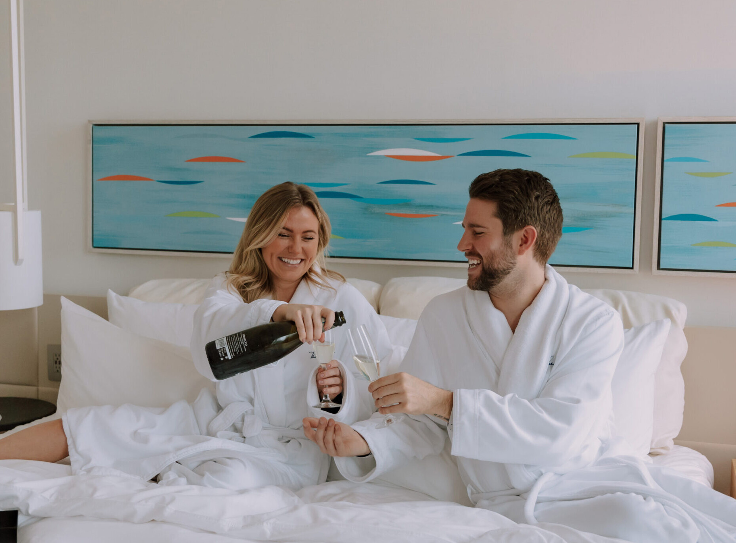 A couple drinking champaign in white robes in bed